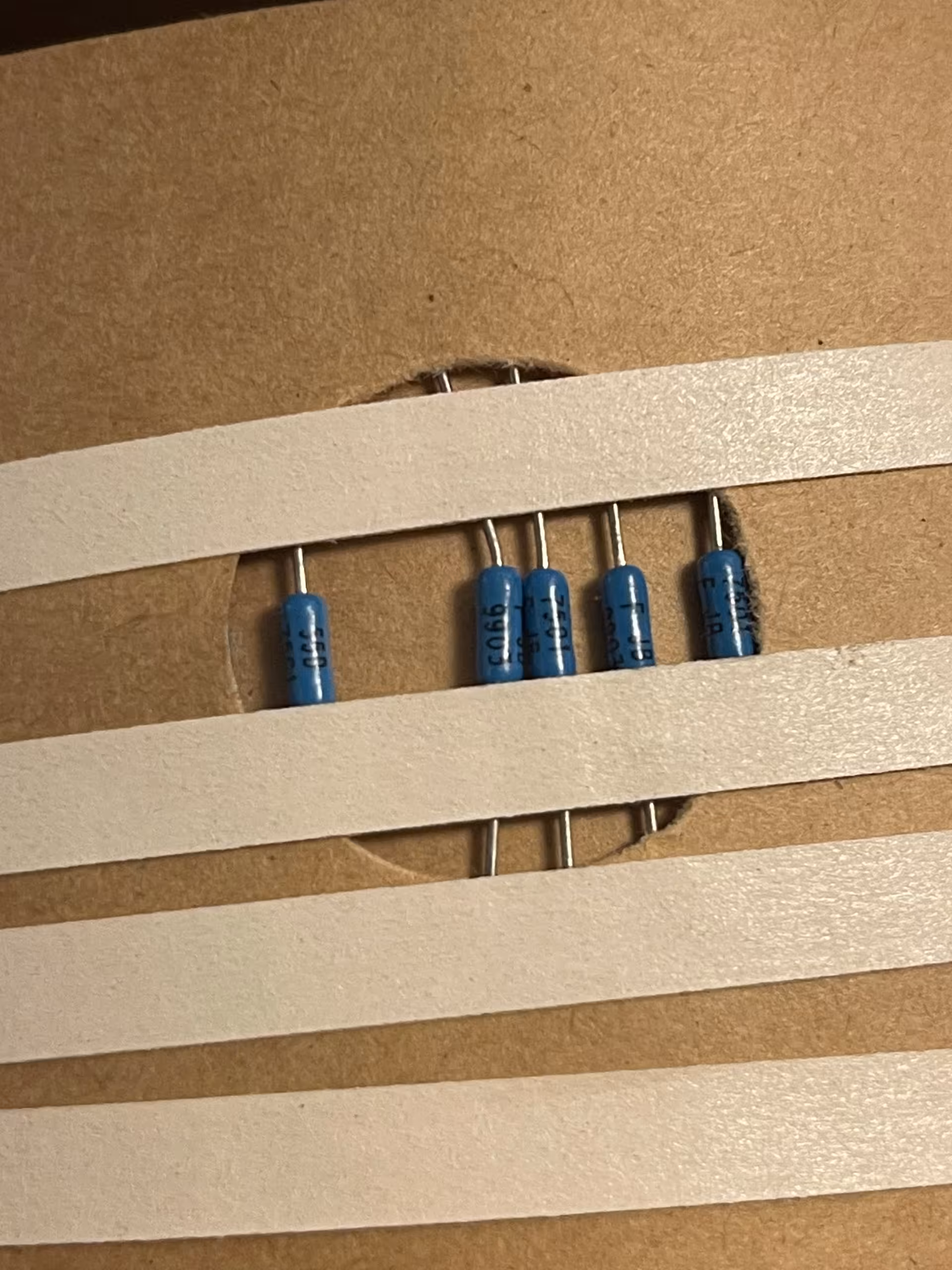 Five blue axial resistors banded between white paper tape strips on kraft board, print 55D, 7501 and 9903