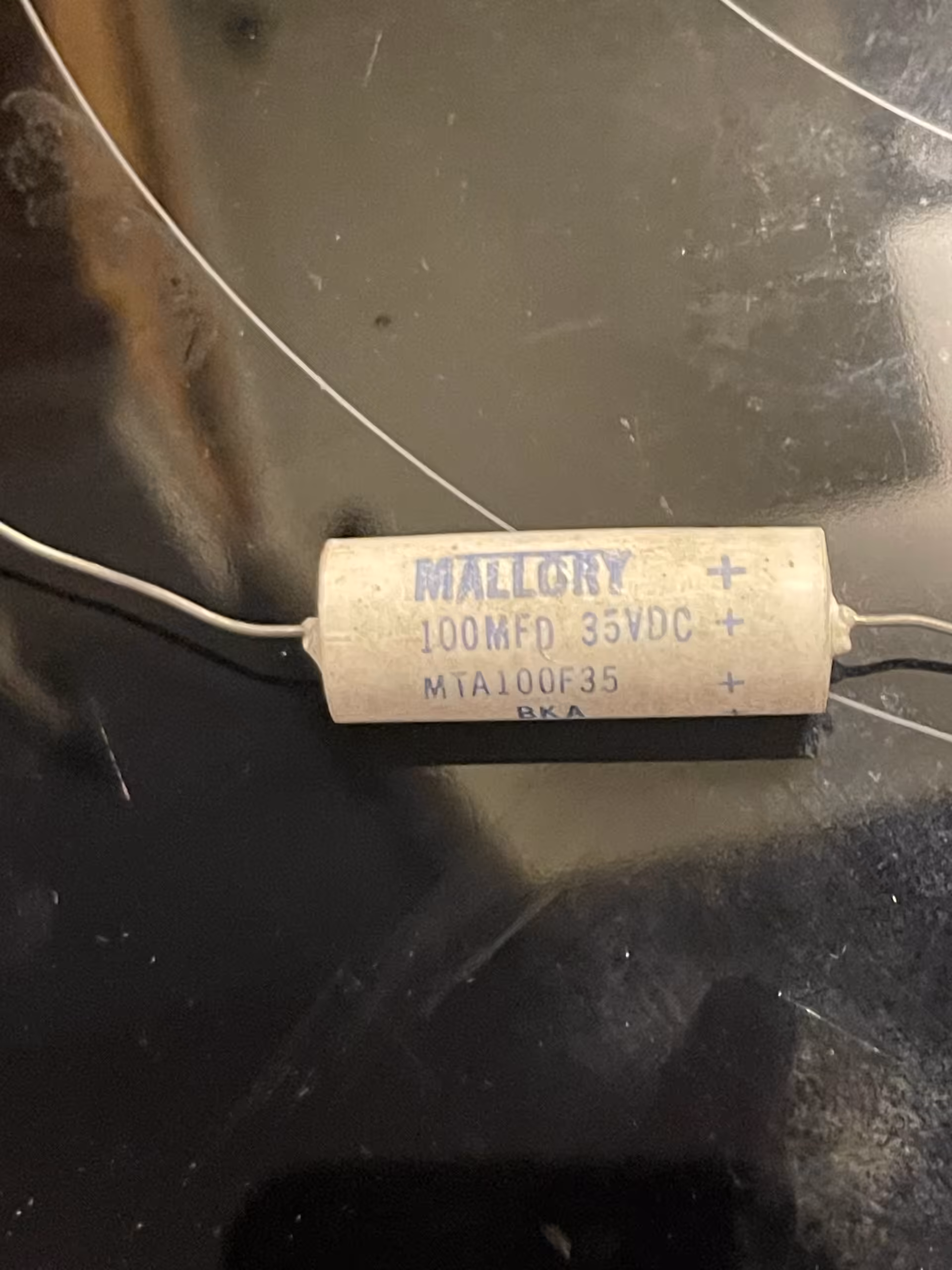 Cream axial electrolytic on black glass, blue print: MALLORY 100MFD 35VDC MTA100F35 BKA, plus marks.