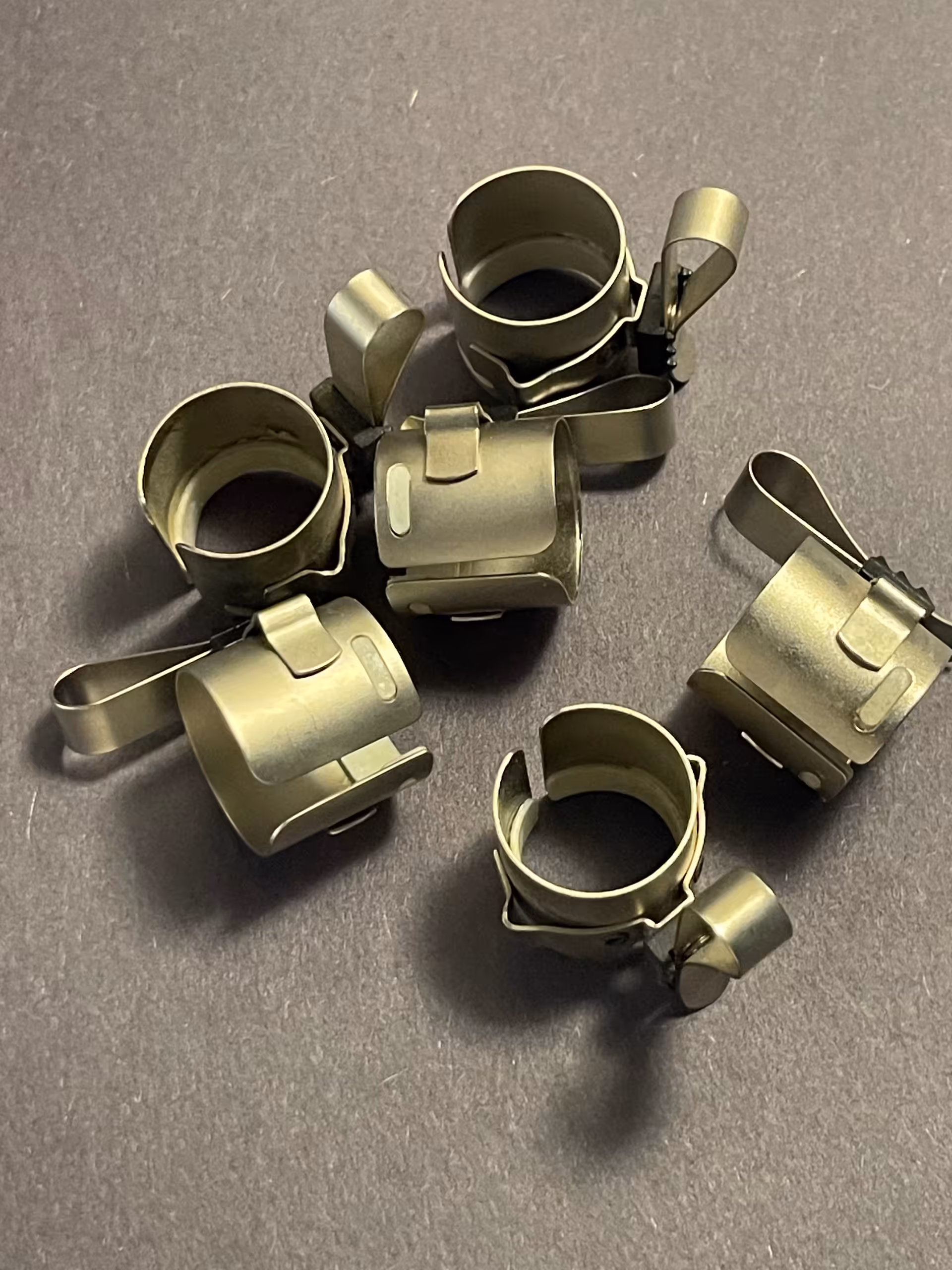 Six unmarked spring band clamps in bare metal, each a split collar with a lever arm and side terminal.